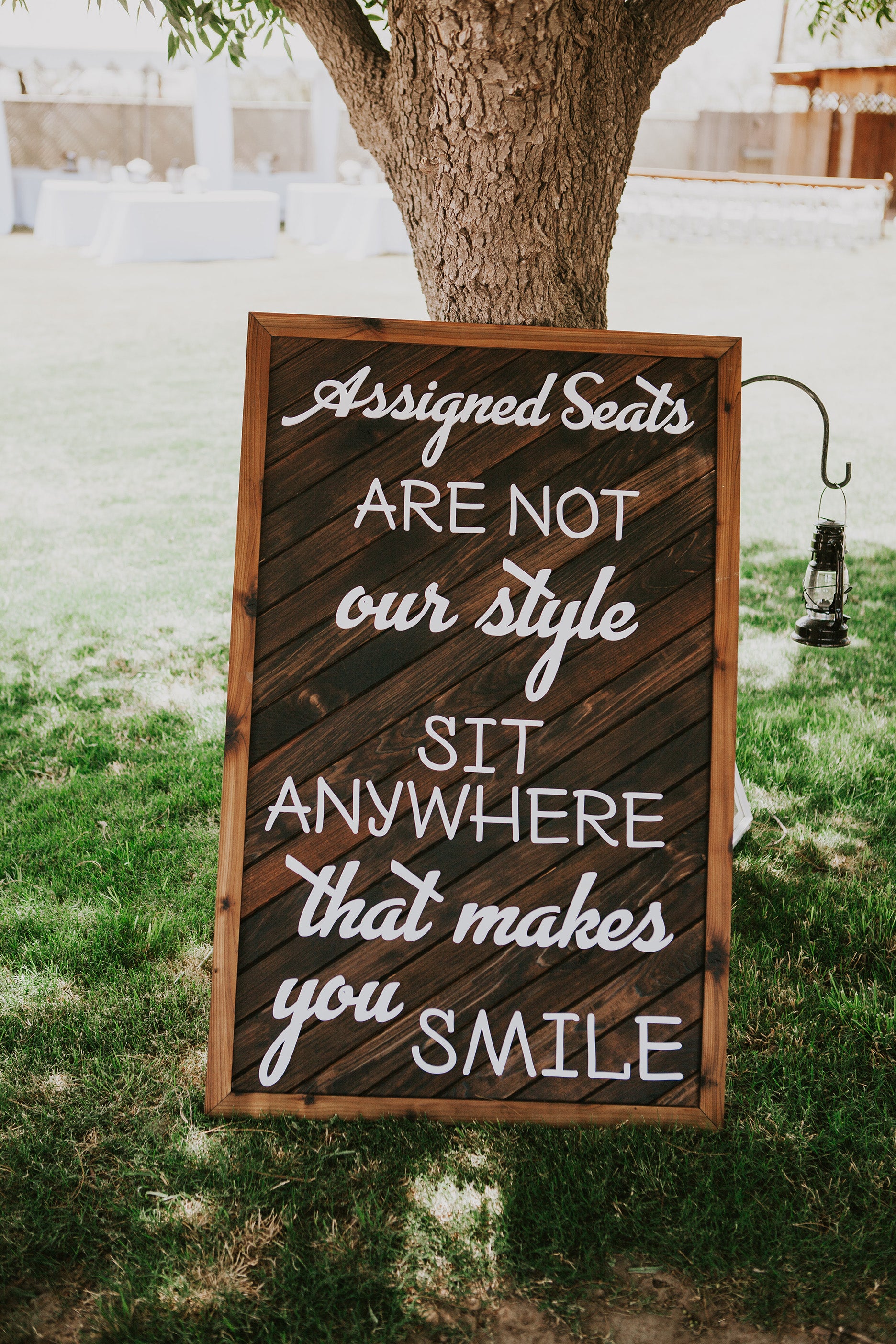 Custom wood sign for weddings, "Assigned seats are not our style, sit anywhere that makes you smile." This custom wood sign is made out of a red cedar backing and white cedar frame. The patterned backing is made from reclaimed cedar. Are you interested in a custom wood sign for your wedding venue? Please visit our shop or fill out the contact us form for a quote. 